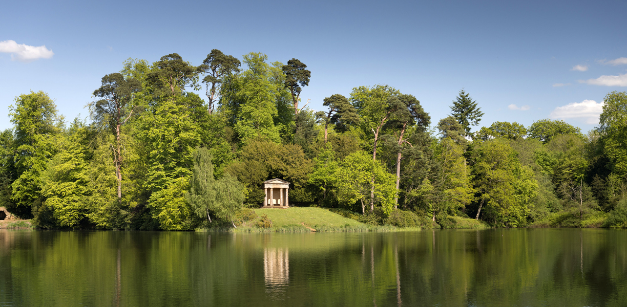 A small stone building reflected in the water at the edge of a lake