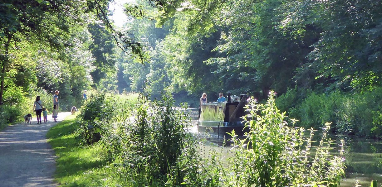 People walk next to the canal with green trees all around