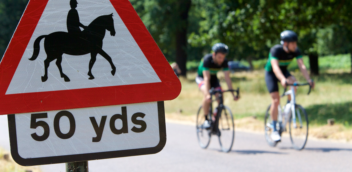 Two cyclists ride past a horse-and-rider sign