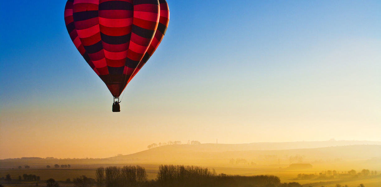red hot air balloon floating above misty landscape
