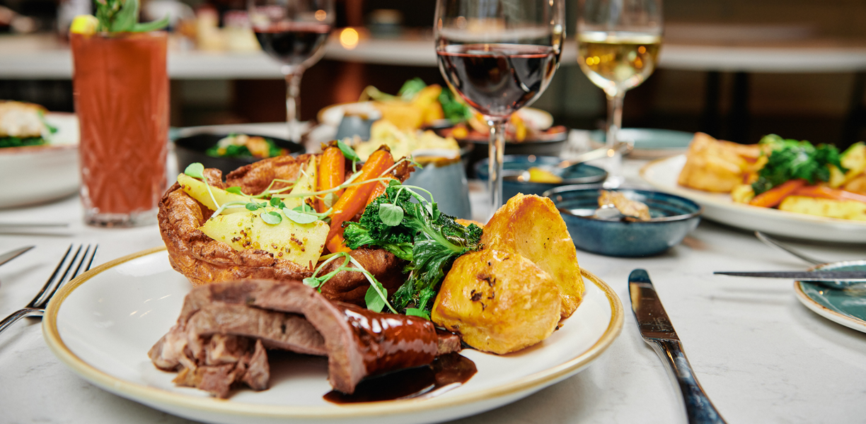 plate with roast dinner next to glasses of wine and cocktails