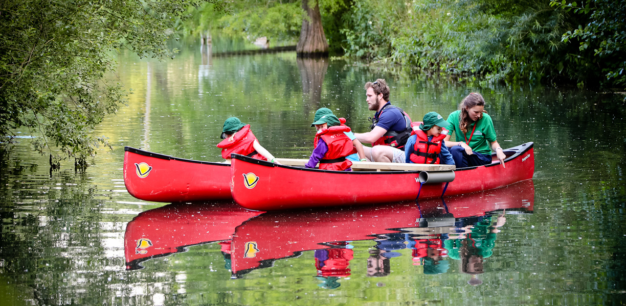 Children and adults in a pair of red canoes on the river