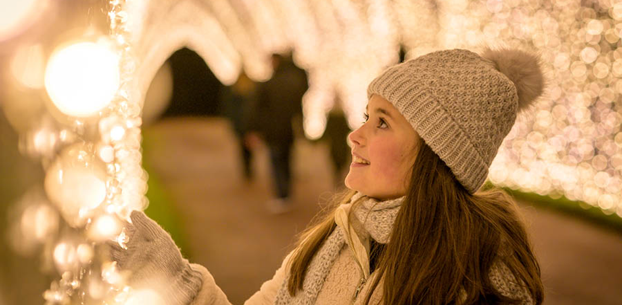 girl in gloves reaching out to sparkling christmas lights