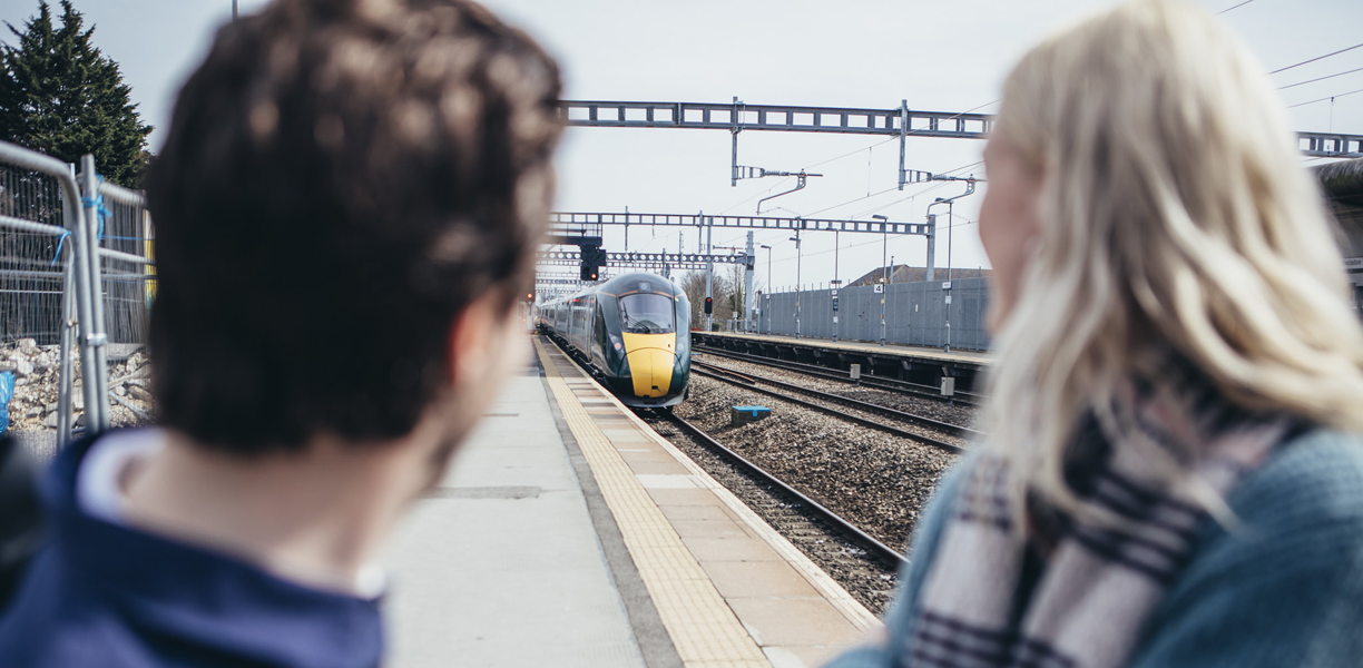A man and a woman wait on a platform for the train